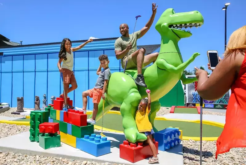 family posing with giant dinosaur toy at Toy Box Mini Golf